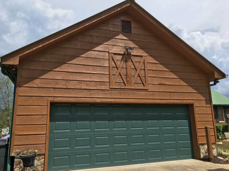 Detached garage with wood siding stained cedar brown and a green garage door